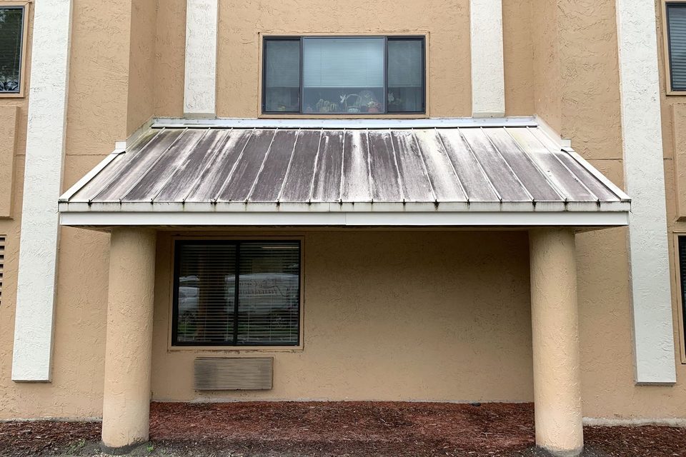 A metal awning on a commercial building, streaked dark with mildew