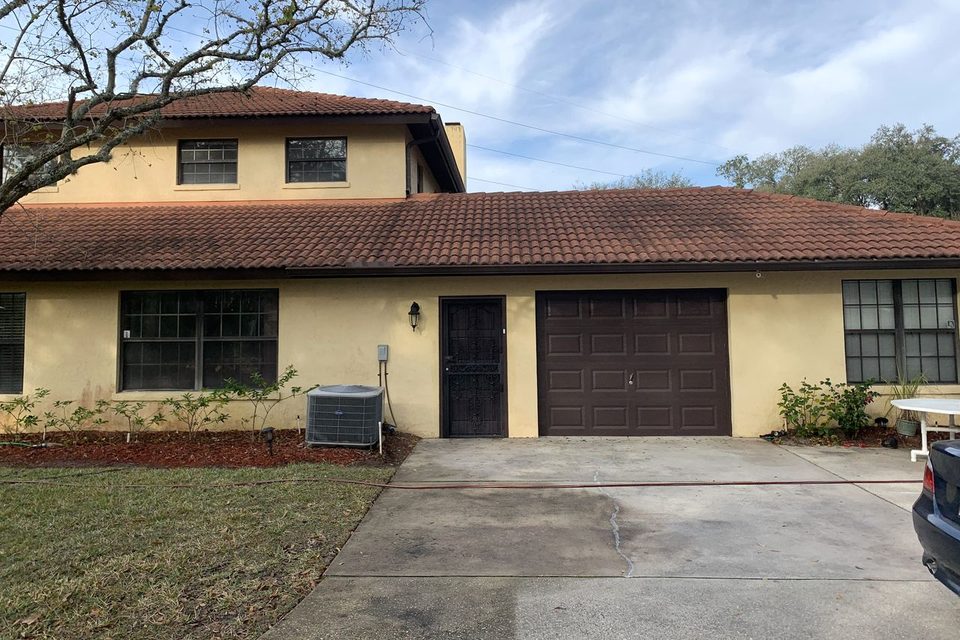 A stucco house with a tile roof dark with mildew and the driveway half washed