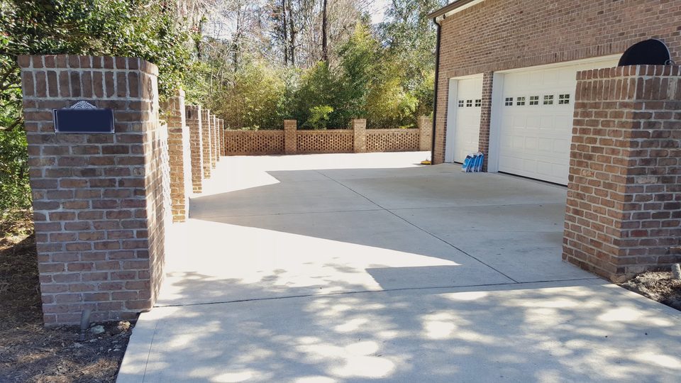A clean concrete driveway running between brick posts toward a garage