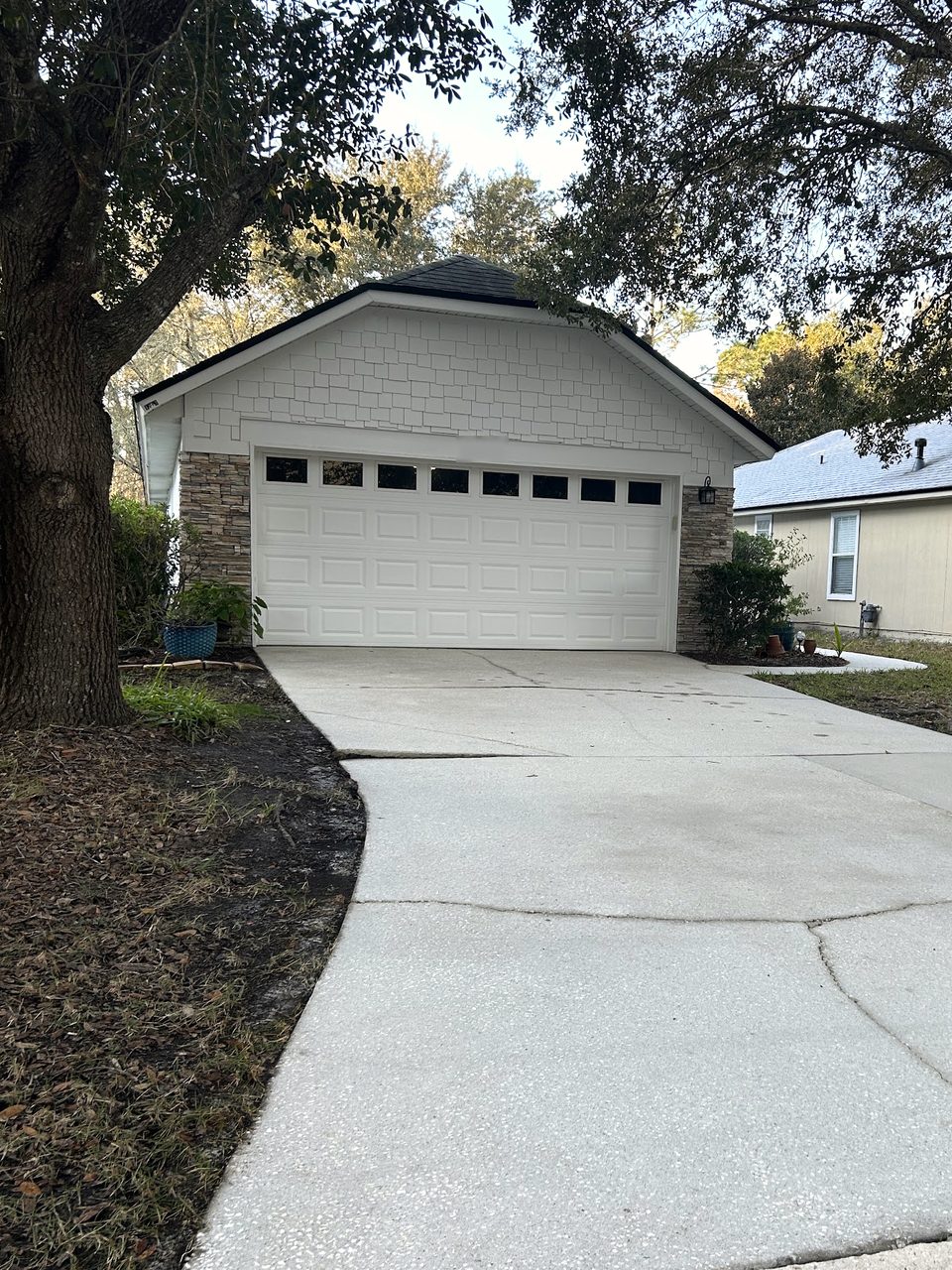Freshly washed concrete driveway leading to a garage under oak trees