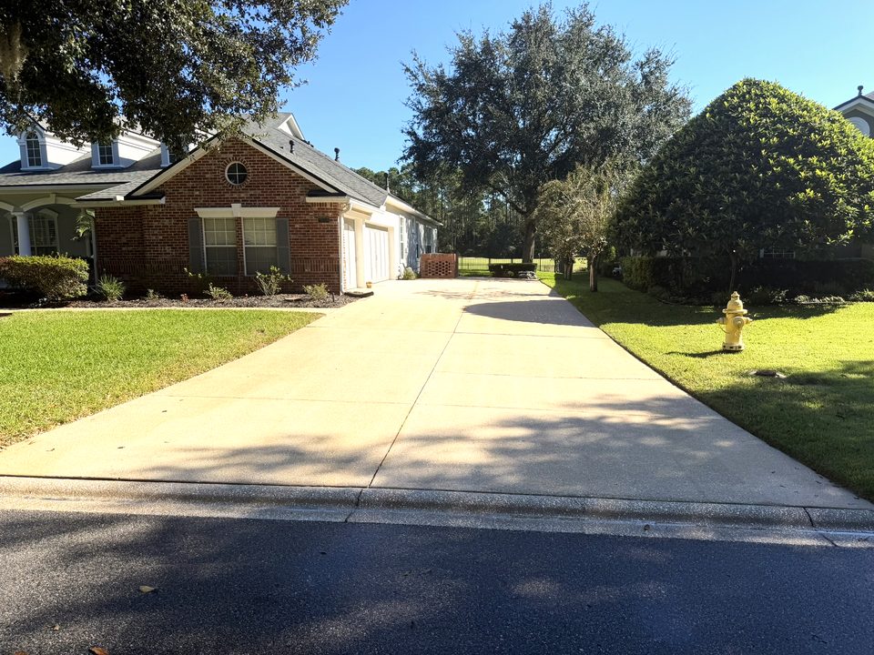 Long concrete driveway under live oaks after a wash, leading up to a brick house
