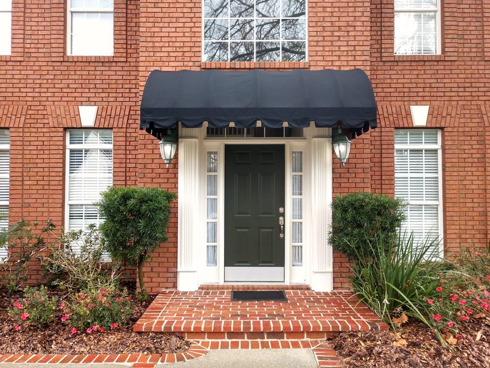A brick front entry with a dark awning and red brick steps after a house wash