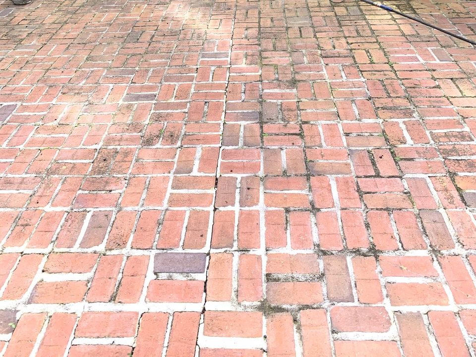 A brick walkway dull with dirt and moss in the joints