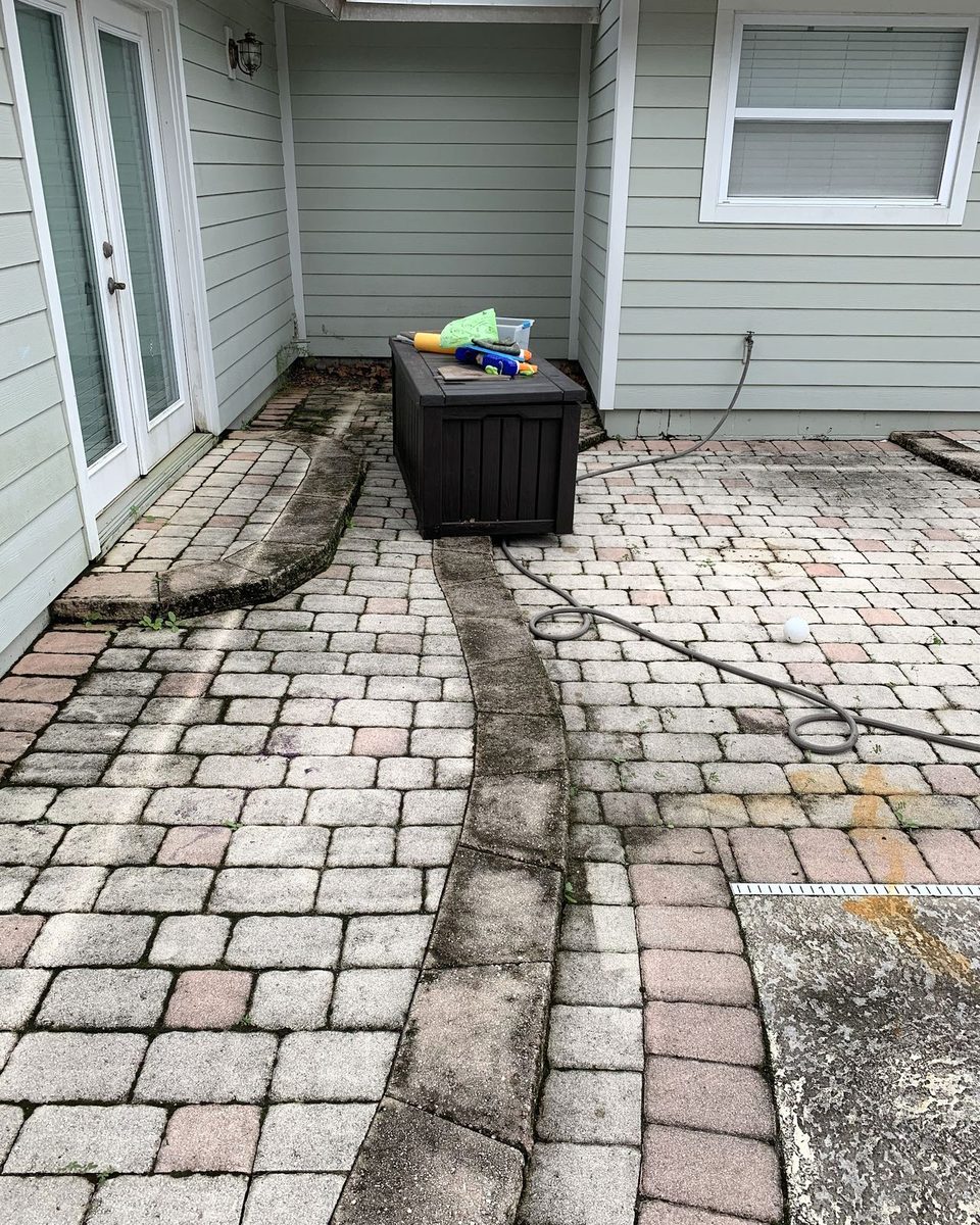 A paver patio beside a house, dark with mildew along the borders