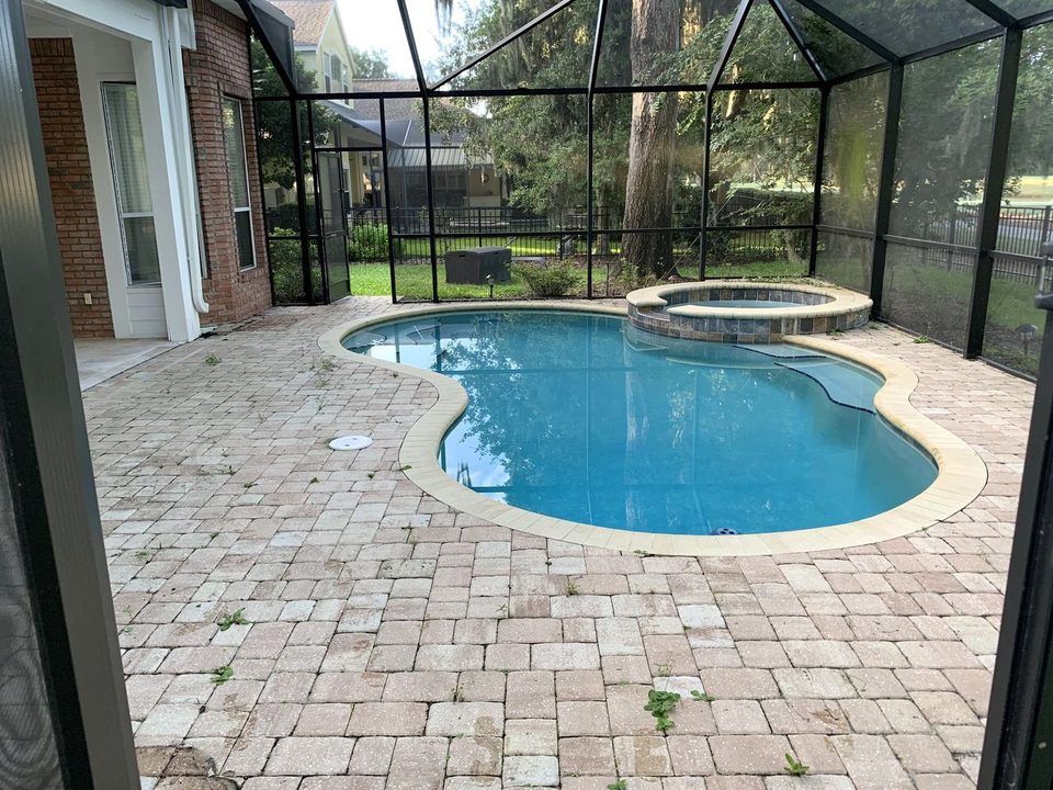 A paver pool deck inside a screen enclosure, gray with weeds in the joints