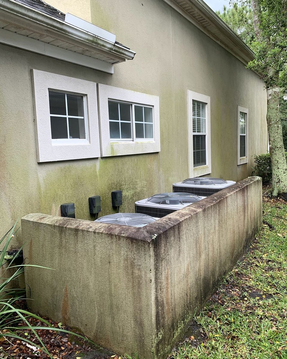A stucco wall and the low wall around the AC units, green and black with mildew