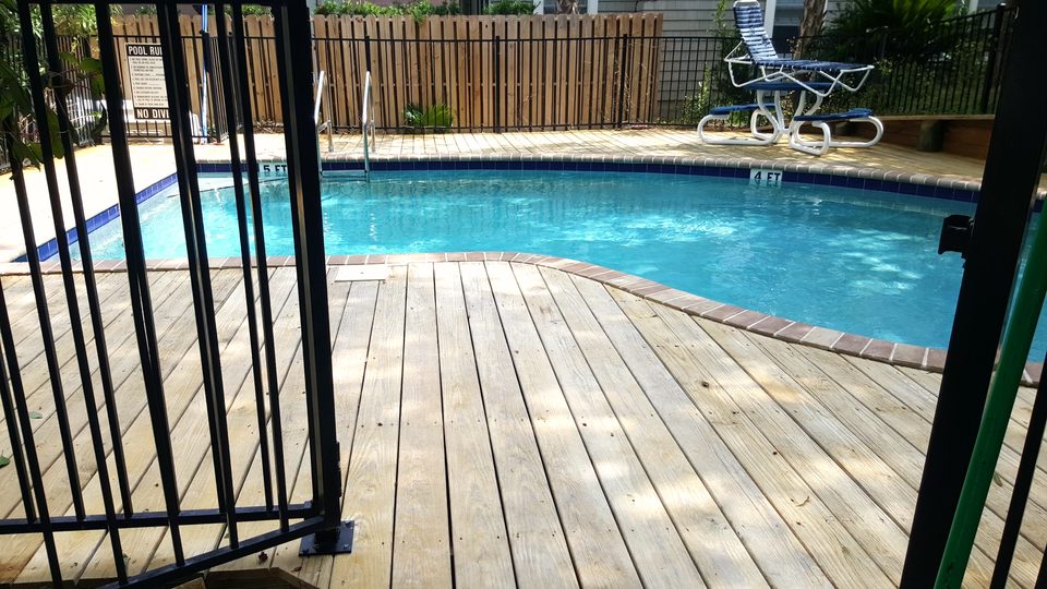 Wood pool deck and in-ground pool behind a black fence after a wash